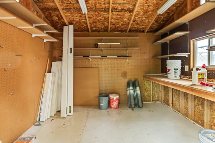 Utility room featuring extensive pegboard walls, abundant open shelving, a built-in workbench, and a window for natural light
