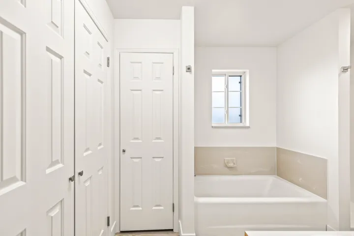 Clean white bathtub with beige half-wall tile surround and a frosted window