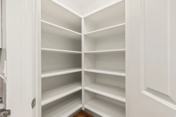 Corner pantry featuring multiple white built-in shelves and a wood-finish floor
