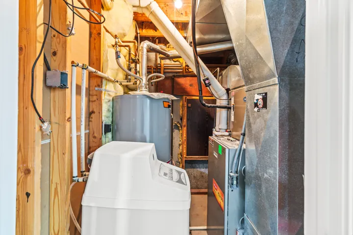 Utility closet featuring a water heater, water softener, and HVAC system with exposed ductwork and electrical wiring