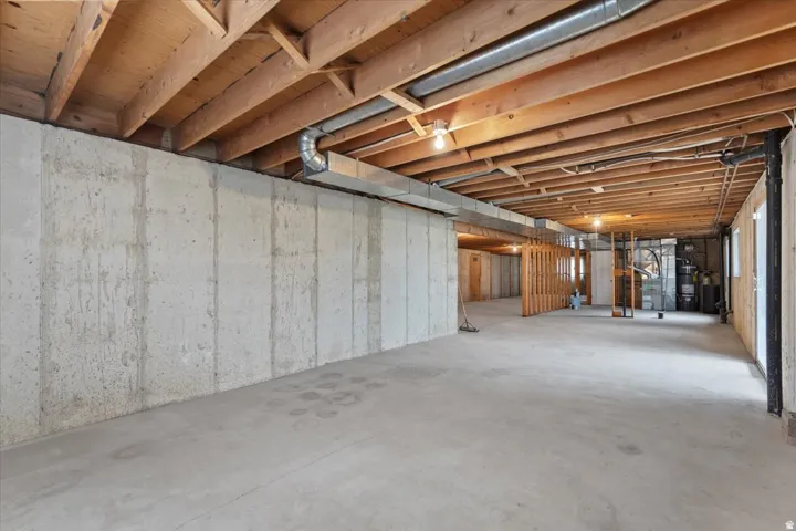 Expansive concrete floor basement with exposed wooden joists and concrete walls, featuring ductwork and plumbing