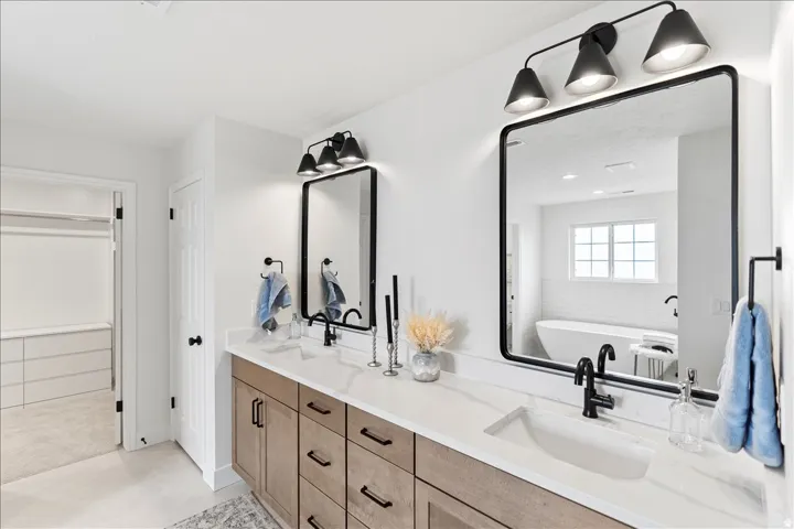 Dual vanity featuring light wood-finish cabinetry, white stone countertops, and matte black hardware
