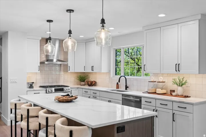 Gourmet kitchen featuring a large central island with seating, white shaker cabinetry, stainless steel appliances, a tile backsplash, and quartz countertops