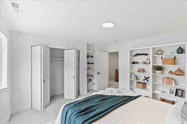 Spacious bedroom featuring light gray carpeting, a built-in shelving unit, and bi-fold closet doors