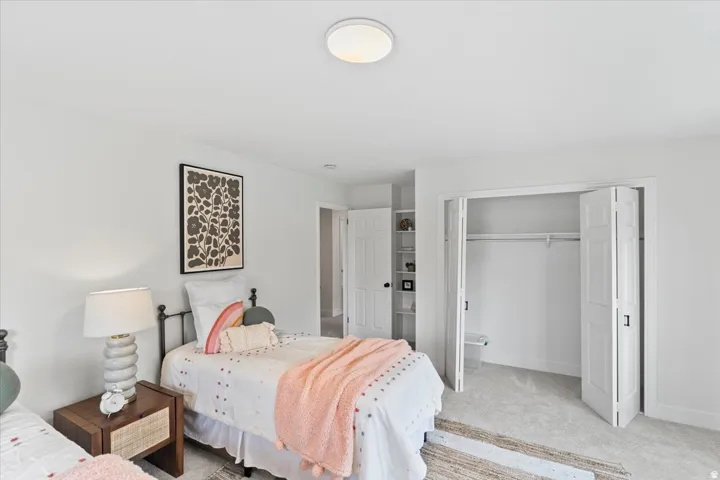 Carpeted room featuring a ceiling-mounted light fixture, white walls, and a bi-fold closet with white paneled doors and black hardware