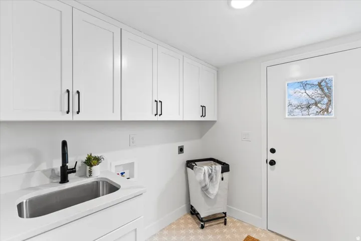 Utility room featuring white shaker-style cabinetry, a stainless steel undermount sink with a matte black faucet, light-toned patterned floor tiling, and a white door with an integrated window