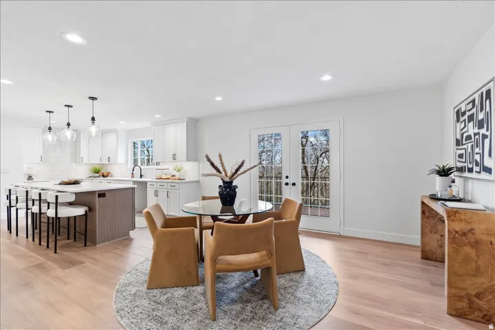 Open-concept kitchen and dining area featuring light wood-finish flooring, white cabinetry, a large kitchen island with seating, a white subway tile backsplash, and French doors
