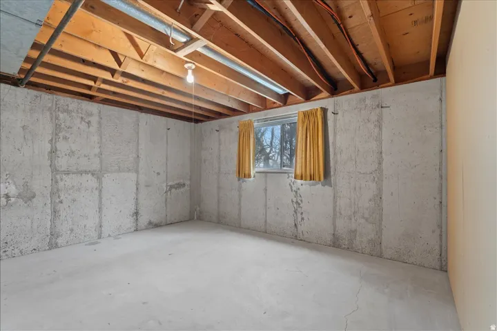 Unfinished basement space featuring exposed wood joists, concrete block walls, and a poured concrete floor