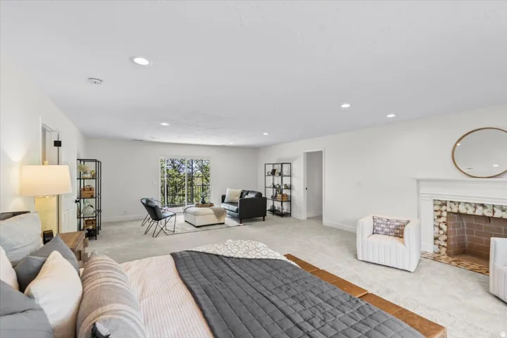 Spacious room featuring light-toned carpeting, recessed lighting, and a fireplace with a white mantel and brick surround