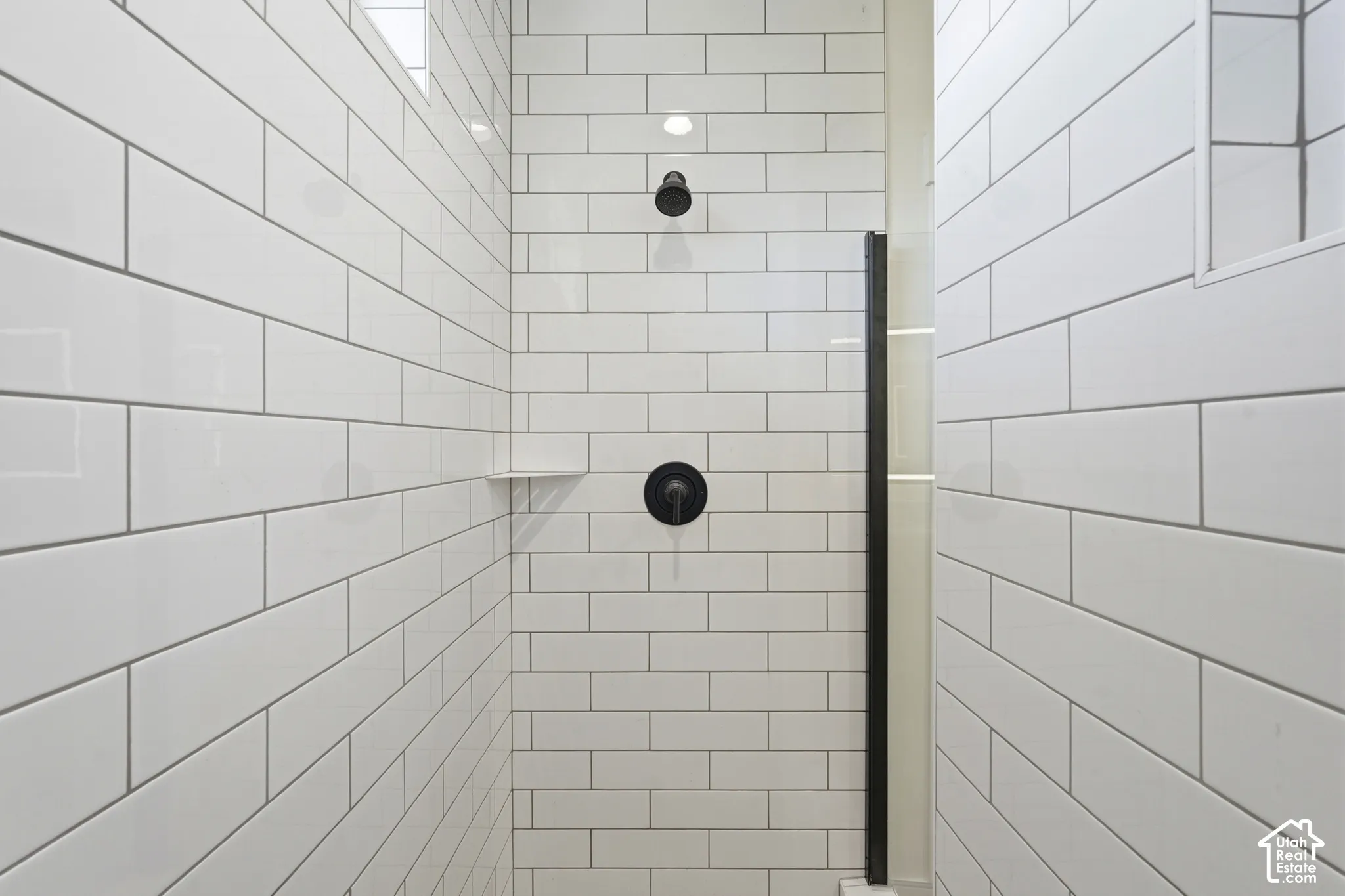 Shower enclosure with white subway tile, matte black fixtures, and a built-in shelf