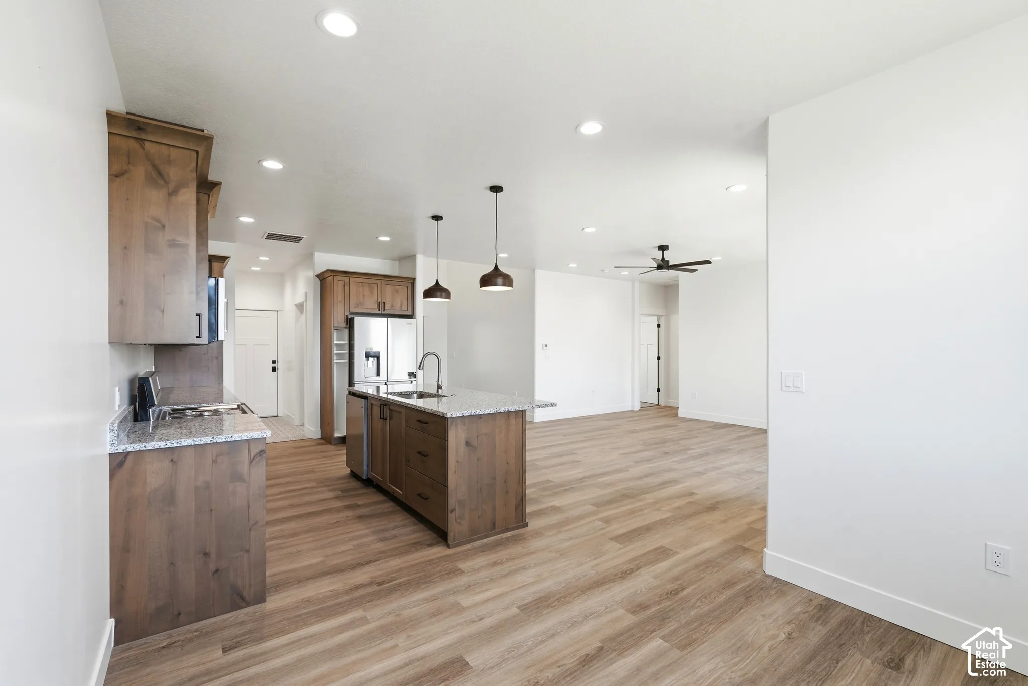Open-concept kitchen featuring wood-finish cabinetry, light-toned countertops, a center island with a sink, stainless steel appliances, and recessed lighting
