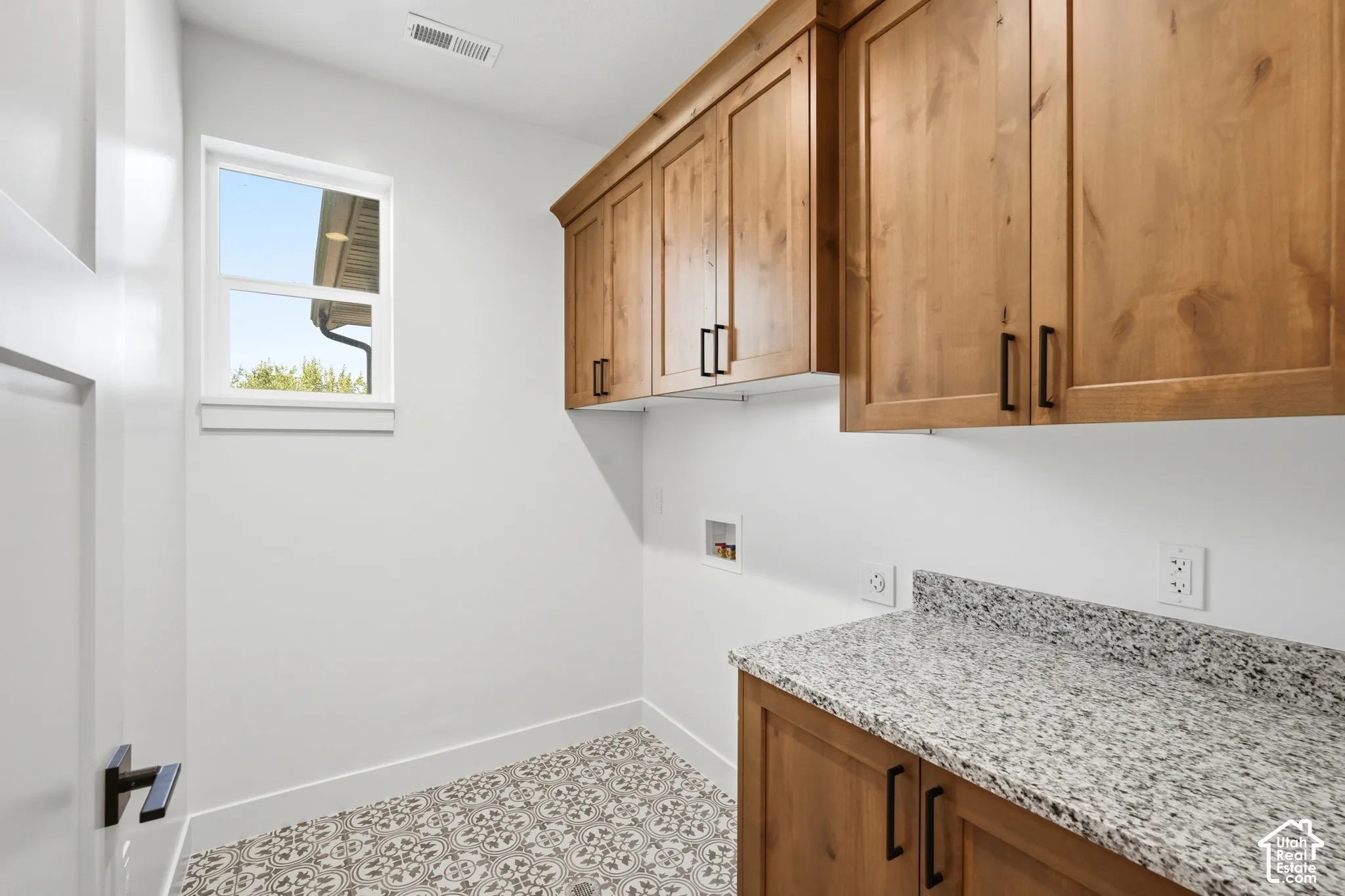 Patterned floor tiling, wood-finish cabinetry with black hardware, and a speckled countertop