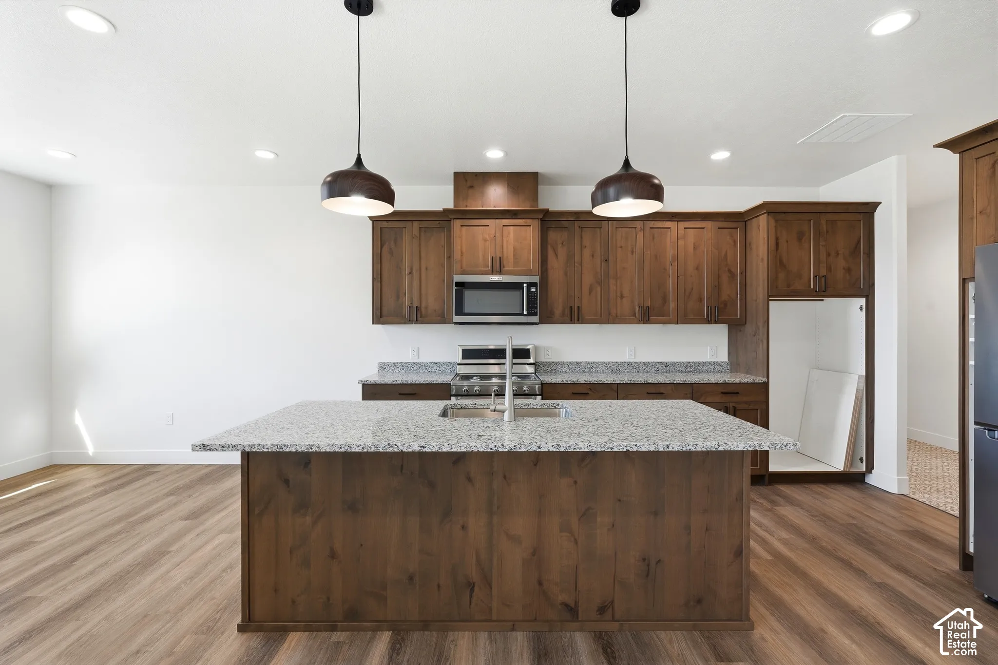 Kitchen featuring a large island with a light-colored countertop, wood-finish cabinetry, stainless steel appliances, and pendant lighting