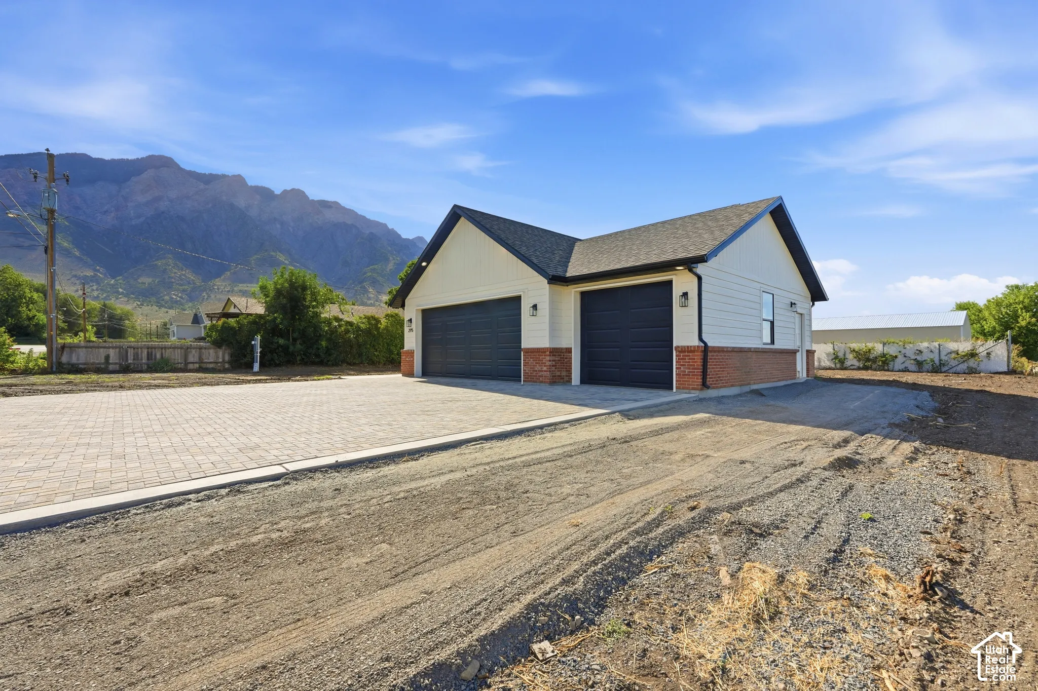Cream siding exterior with brick veneer accent, two dark-toned garage doors, and a paved driveway