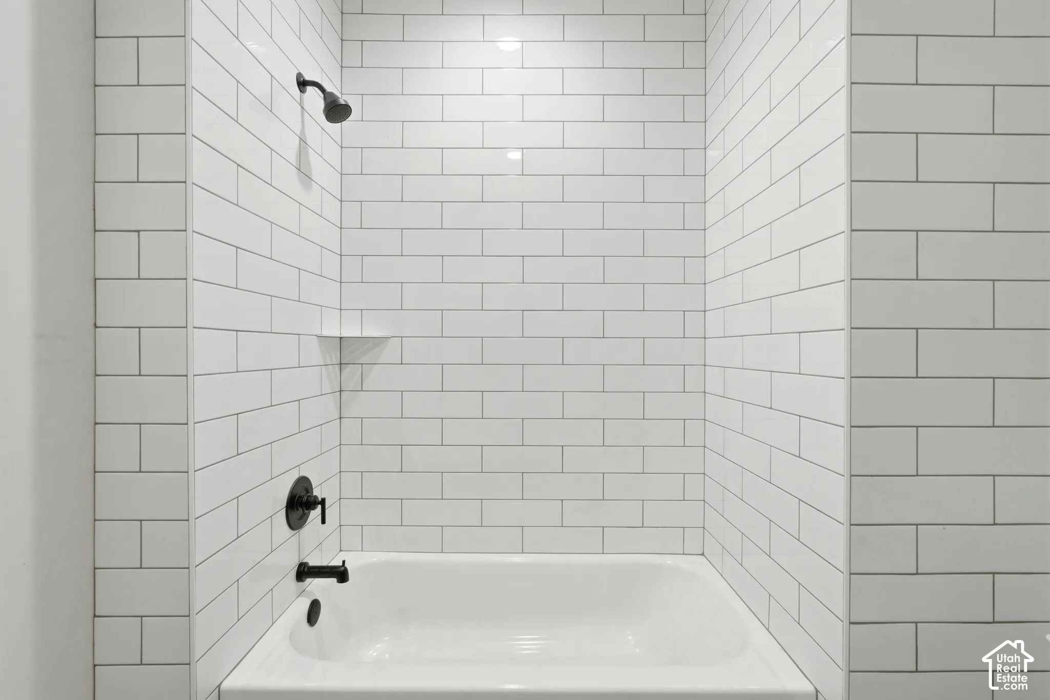 Bathtub with subway tile surround, integrated shelf, and matte black fixtures