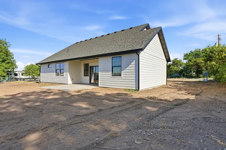 Rear exterior showcasing horizontal siding, a gabled roofline, a concrete patio, and a sliding glass door