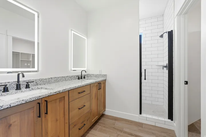 Dual vanity with granite countertops, wood-finish cabinetry, and matte black fixtures