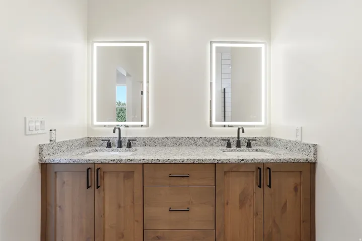 Dual vanities featuring individual lighted mirrors, wood-finish cabinetry, black hardware, and speckled countertops