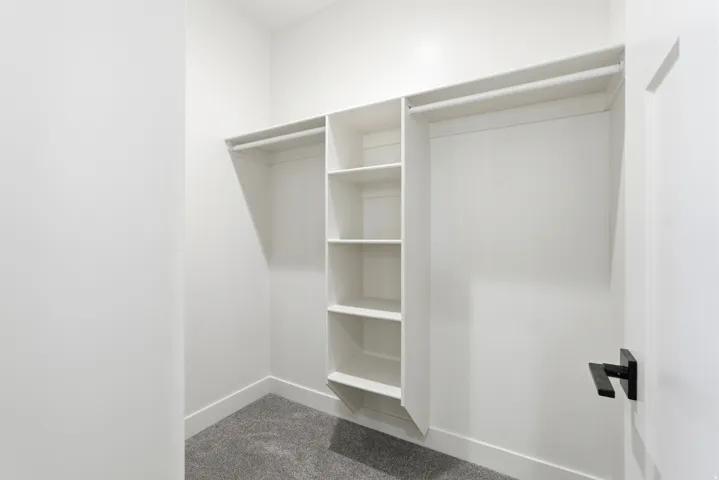 White shelving units, hanging rods, and gray carpeted flooring