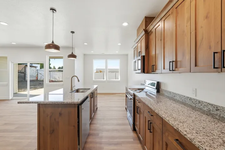 Kitchen featuring wood-finish cabinetry, granite countertops, stainless steel appliances, and a large center island with a sink