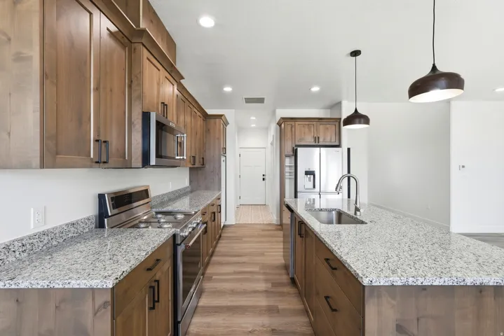 Kitchen featuring wood cabinetry, stainless steel appliances, speckled stone countertops, and wood-finish flooring