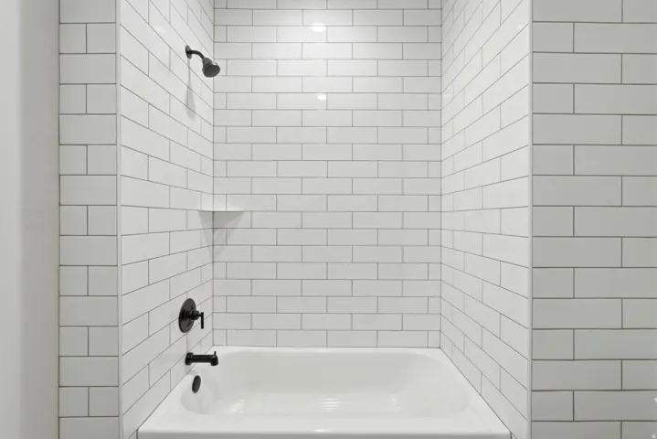 Bathtub with subway tile surround, integrated shelf, and matte black fixtures