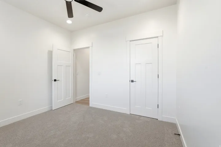 Light gray carpeting with white walls, recessed ceiling lighting, and a ceiling fan