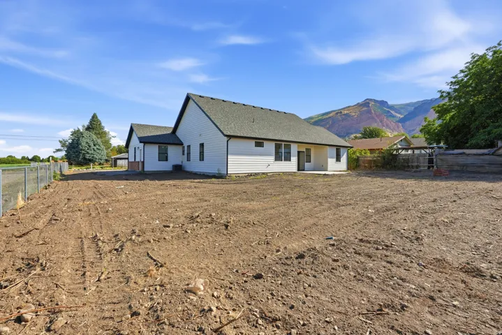 Expansive undeveloped lot with chain-link fencing, featuring a single-story residence with white siding, dark trim, and a patio area