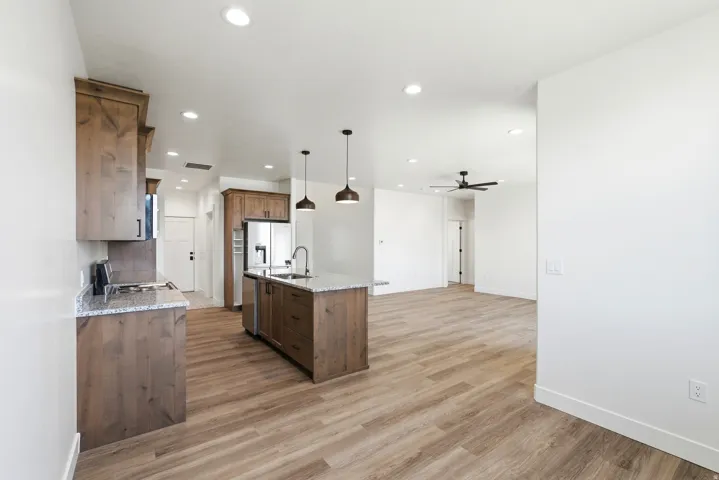 Open-concept kitchen featuring wood-finish cabinetry, light-toned countertops, a center island with a sink, stainless steel appliances, and recessed lighting