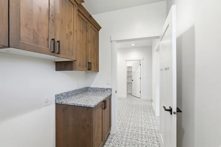 Wood-finish cabinetry with black hardware, speckled countertop, and patterned floor tile