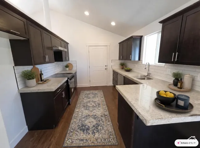 Kitchen featuring dark wood-finish cabinetry, light-toned countertops, a subway tile backsplash, a stainless steel double basin sink with a gooseneck faucet, and a stainless steel dishwasher