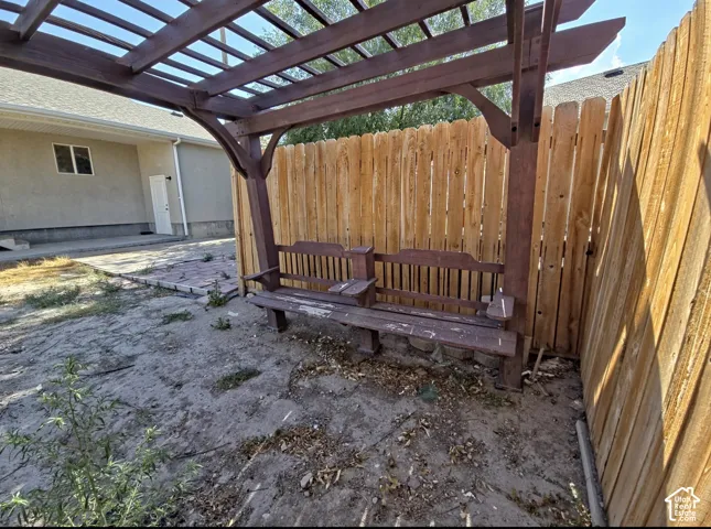 Backyard featuring a wooden pergola with an integrated bench, a wood privacy fence, and a stucco exterior wall with a white door and window