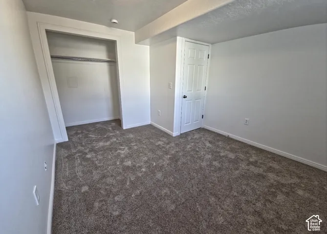 Interior room featuring a neutral color palette, grey patterned carpet, white baseboards, and a white six-panel door
