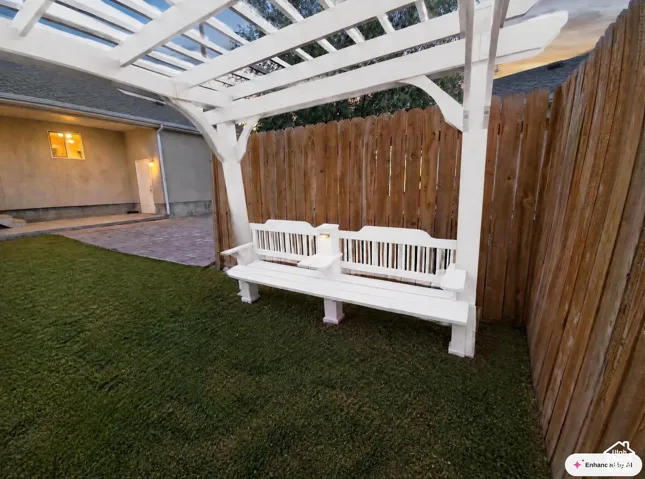 Backyard featuring a wooden pergola with an integrated bench, a wood privacy fence, and a stucco exterior wall with a white door and window