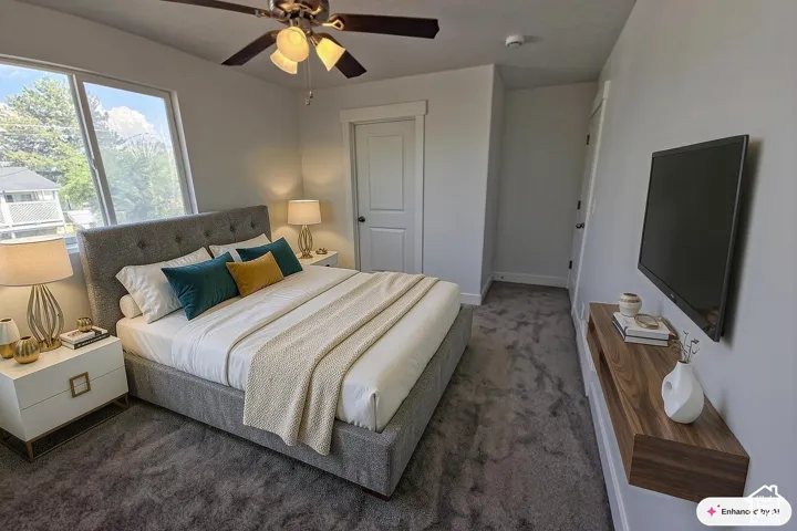 Window with exterior greenery, neutral-toned carpeting, ceiling fan with integrated lighting, wall-mounted wood-finish media shelf