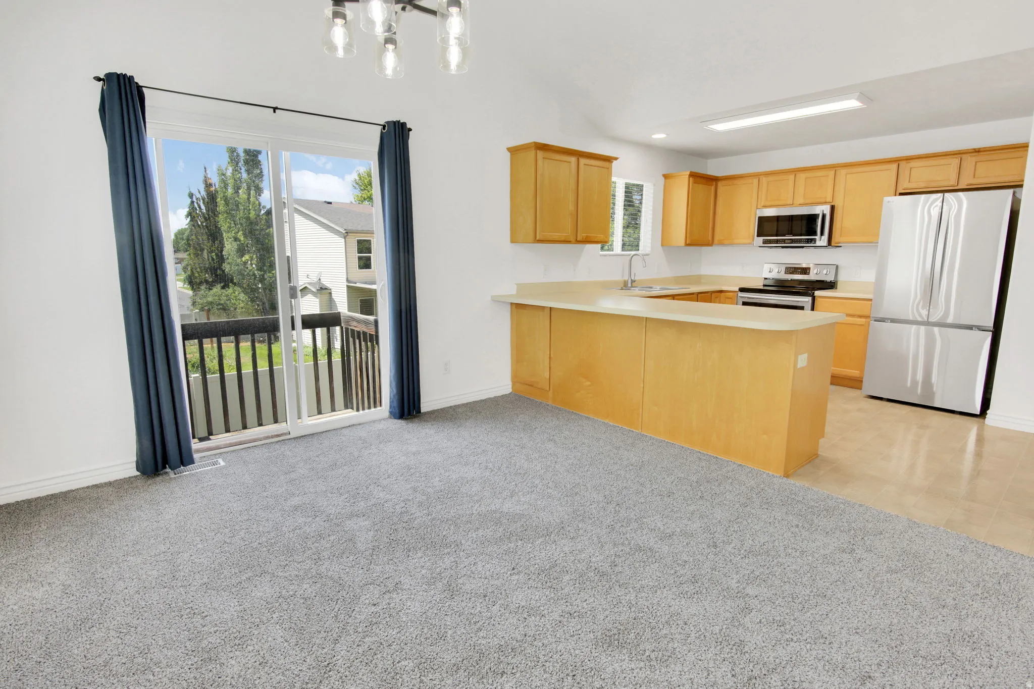 Open-concept living space featuring a kitchen with light wood cabinetry, stainless steel appliances, and a breakfast bar