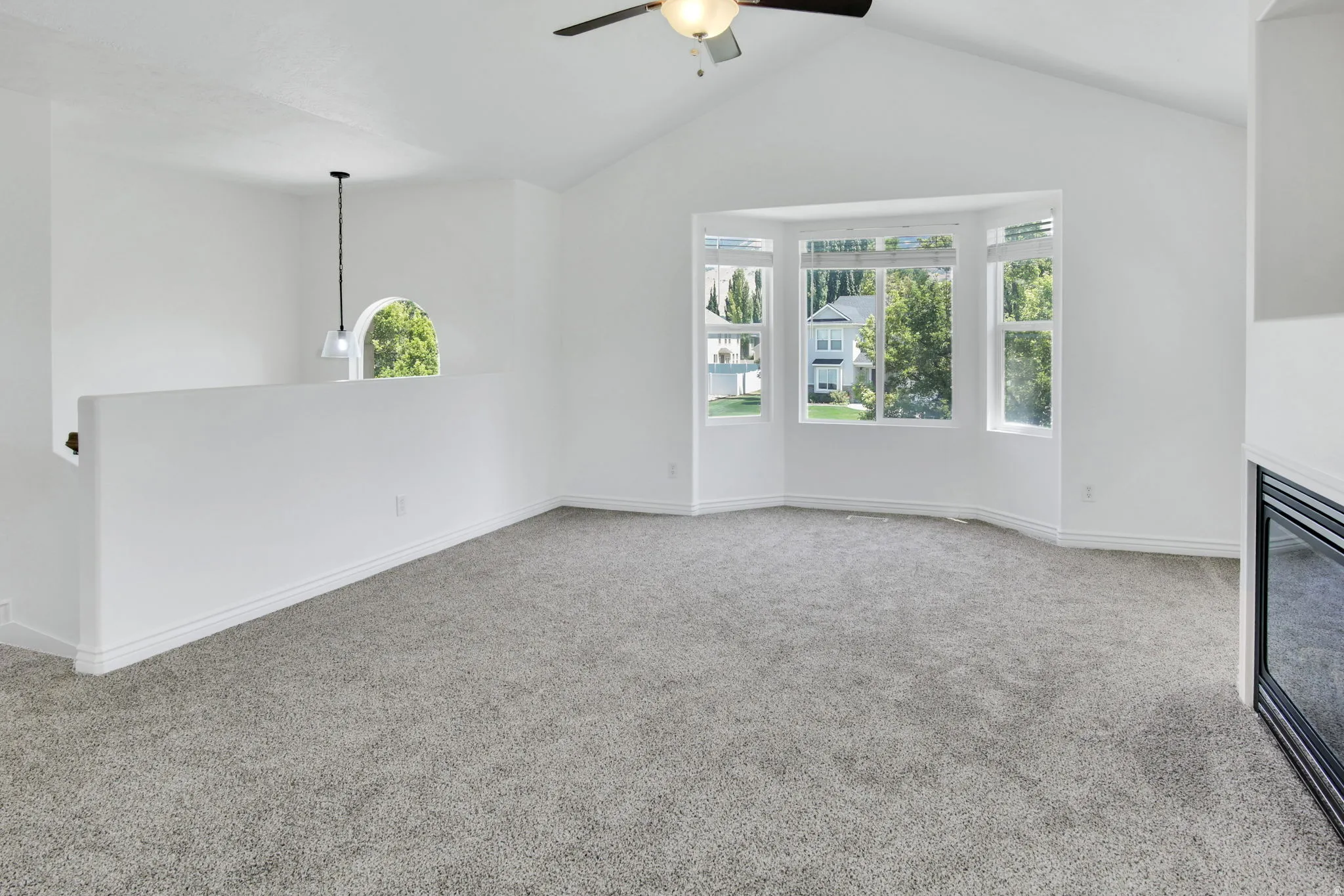 Spacious interior featuring a vaulted ceiling, bay window, light gray carpeting, and a built-in fireplace