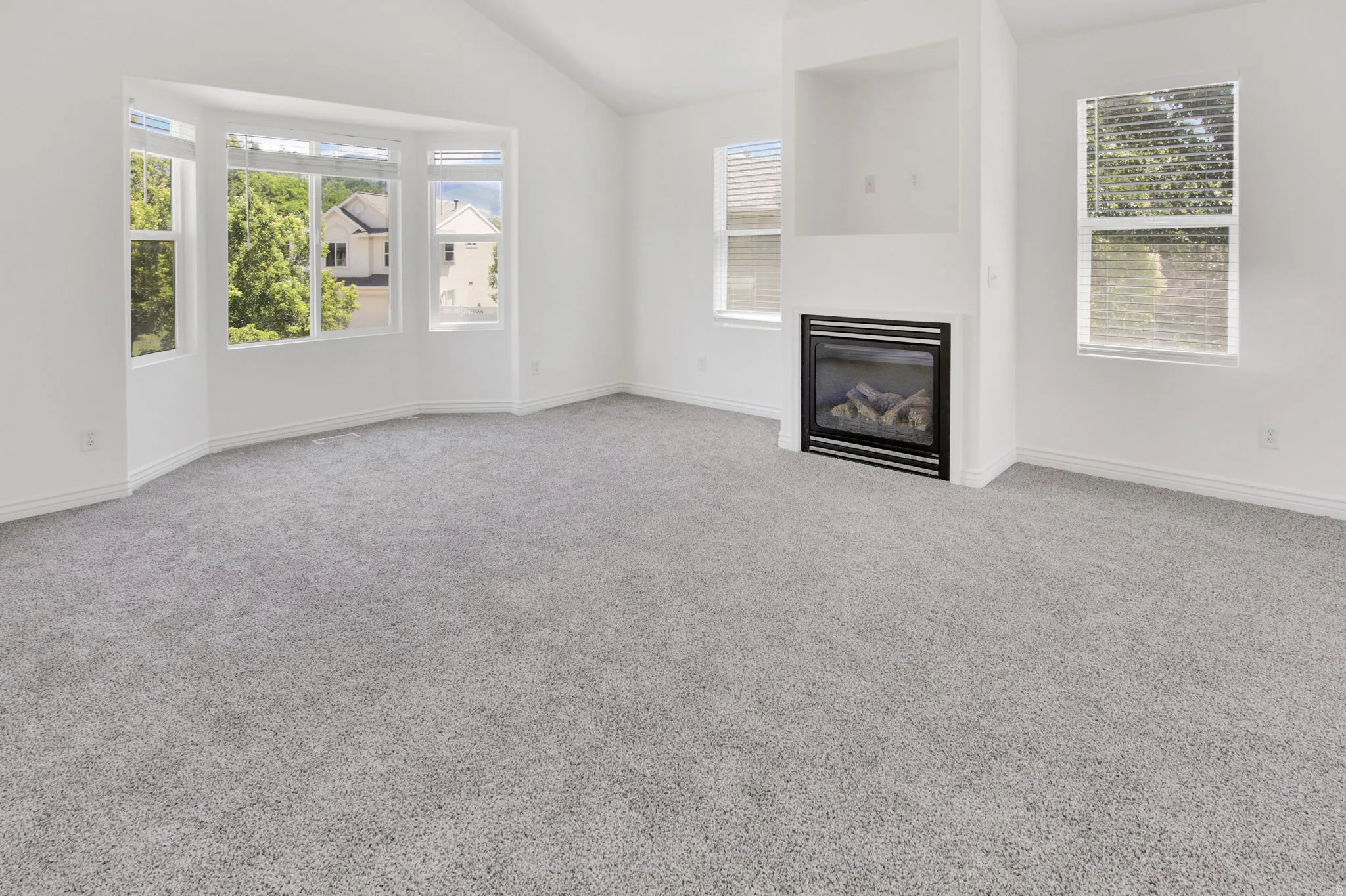 Spacious interior featuring a contemporary fireplace with a black surround, vaulted ceiling, and light gray carpeting