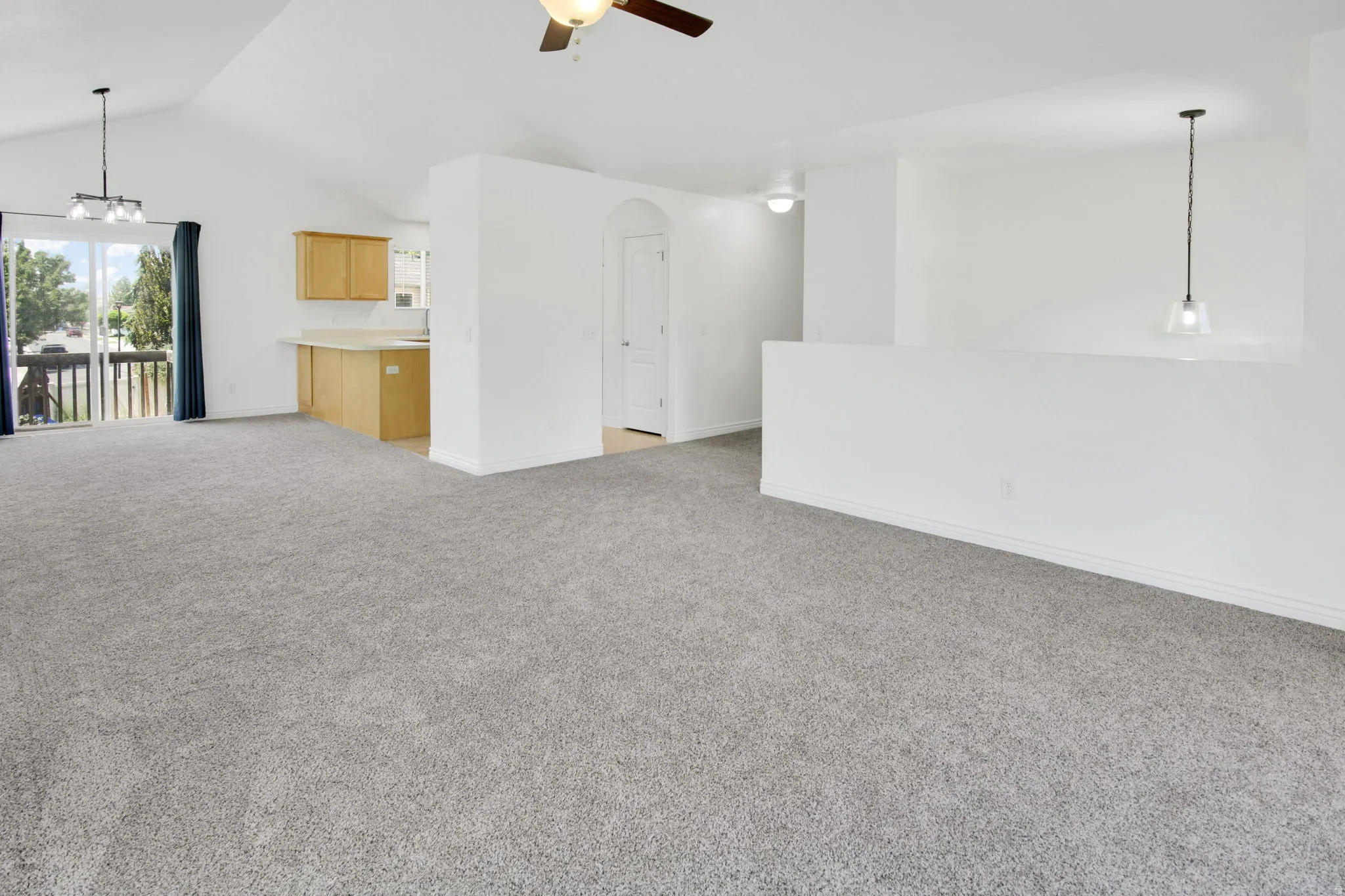 Spacious living area featuring vaulted ceilings, light gray carpet, an overhead ceiling fan, and direct access to an outdoor balcony