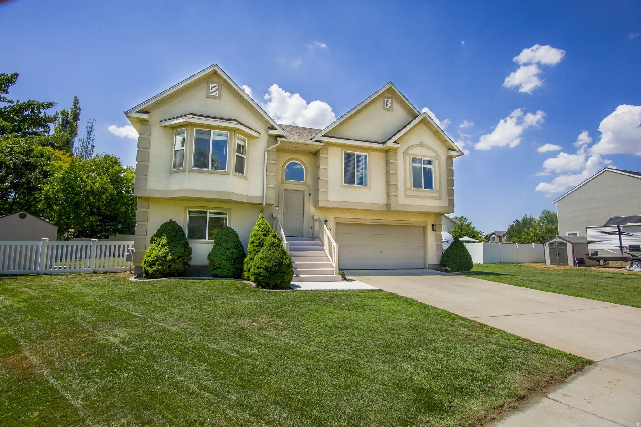Two-story stucco exterior featuring a prominent bay window, attached garage, concrete driveway, and a white picket fence