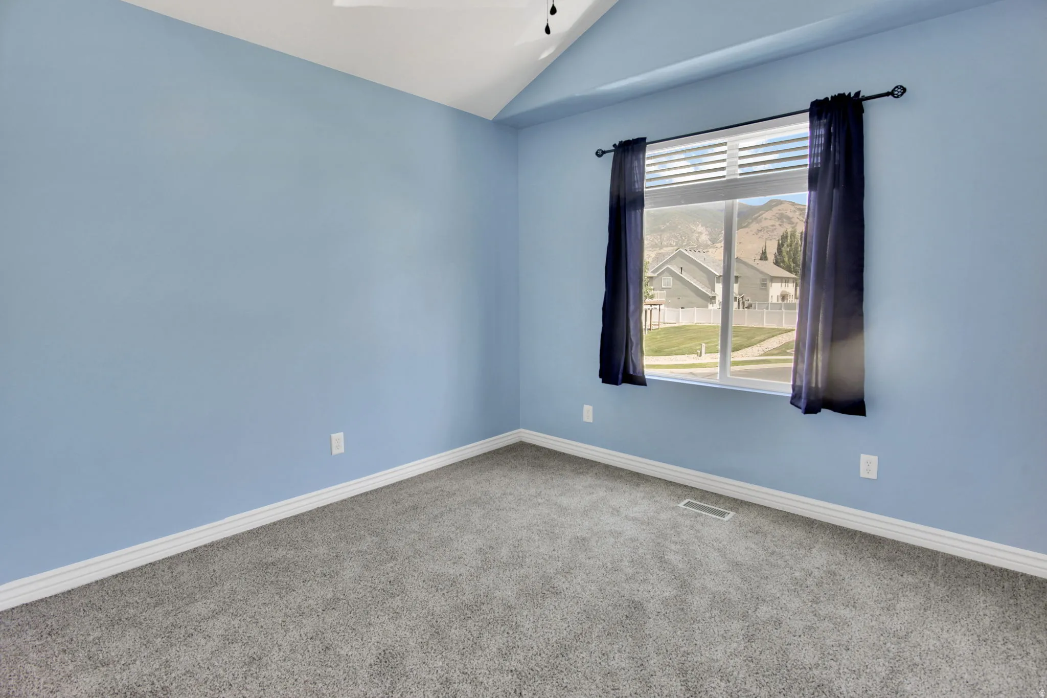 Carpeted room featuring a vaulted ceiling and a window with horizontal blinds and drapery