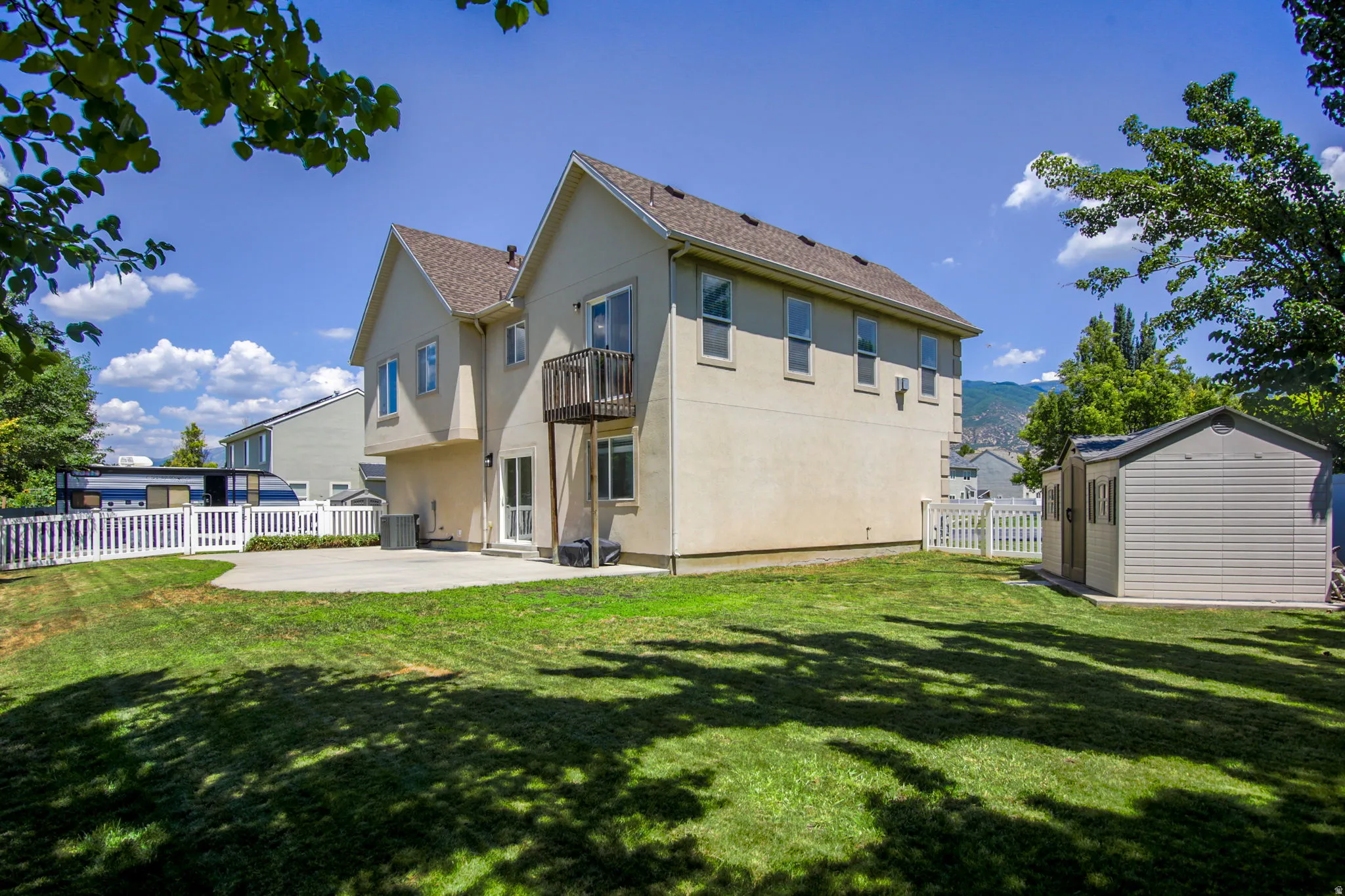 Expansive backyard featuring a large concrete patio, a private second-story balcony, and a dedicated storage shed