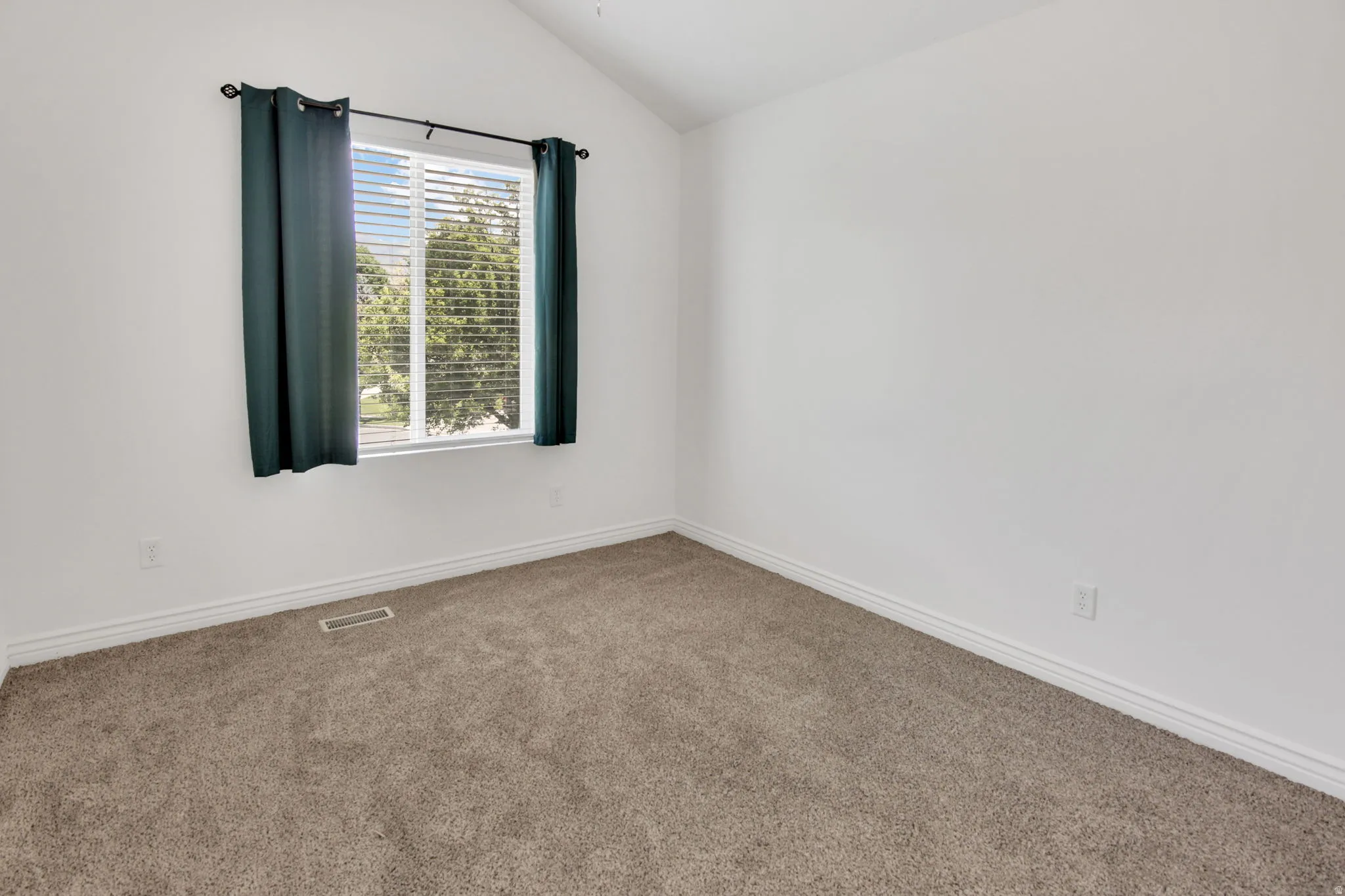 Bright room featuring vaulted ceilings and neutral-toned carpeting