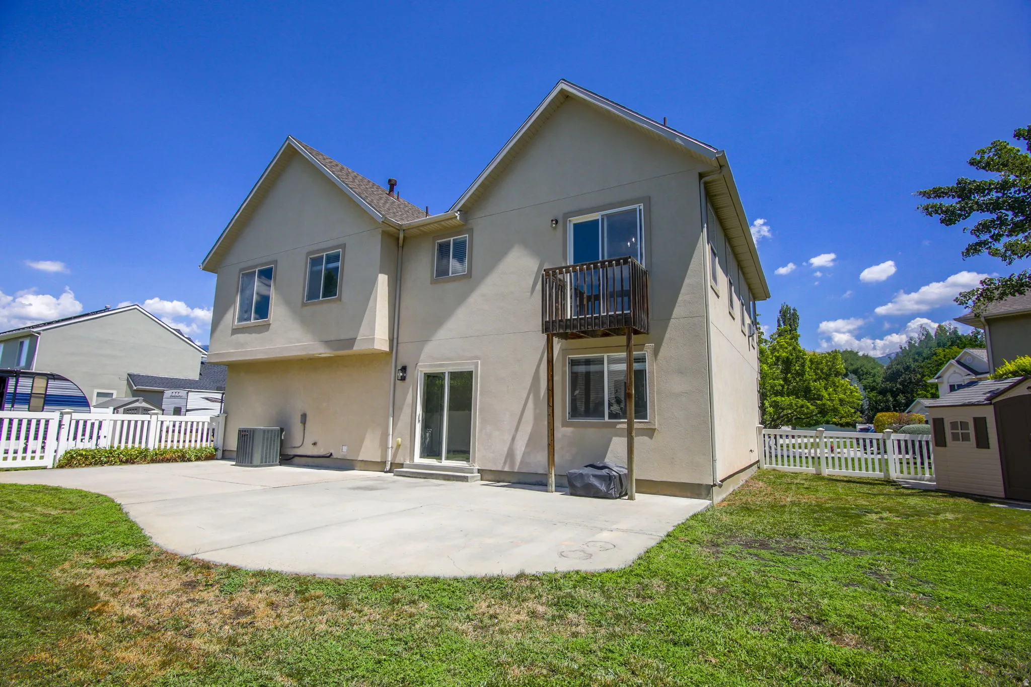 Rear exterior featuring a concrete patio, sliding glass doors, upper balcony, and white picket fencing