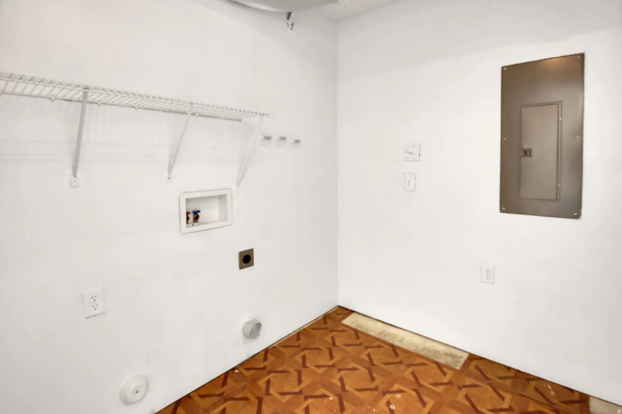 Dedicated utility area featuring a white wire shelving unit, electrical outlet, and a circuit breaker panel