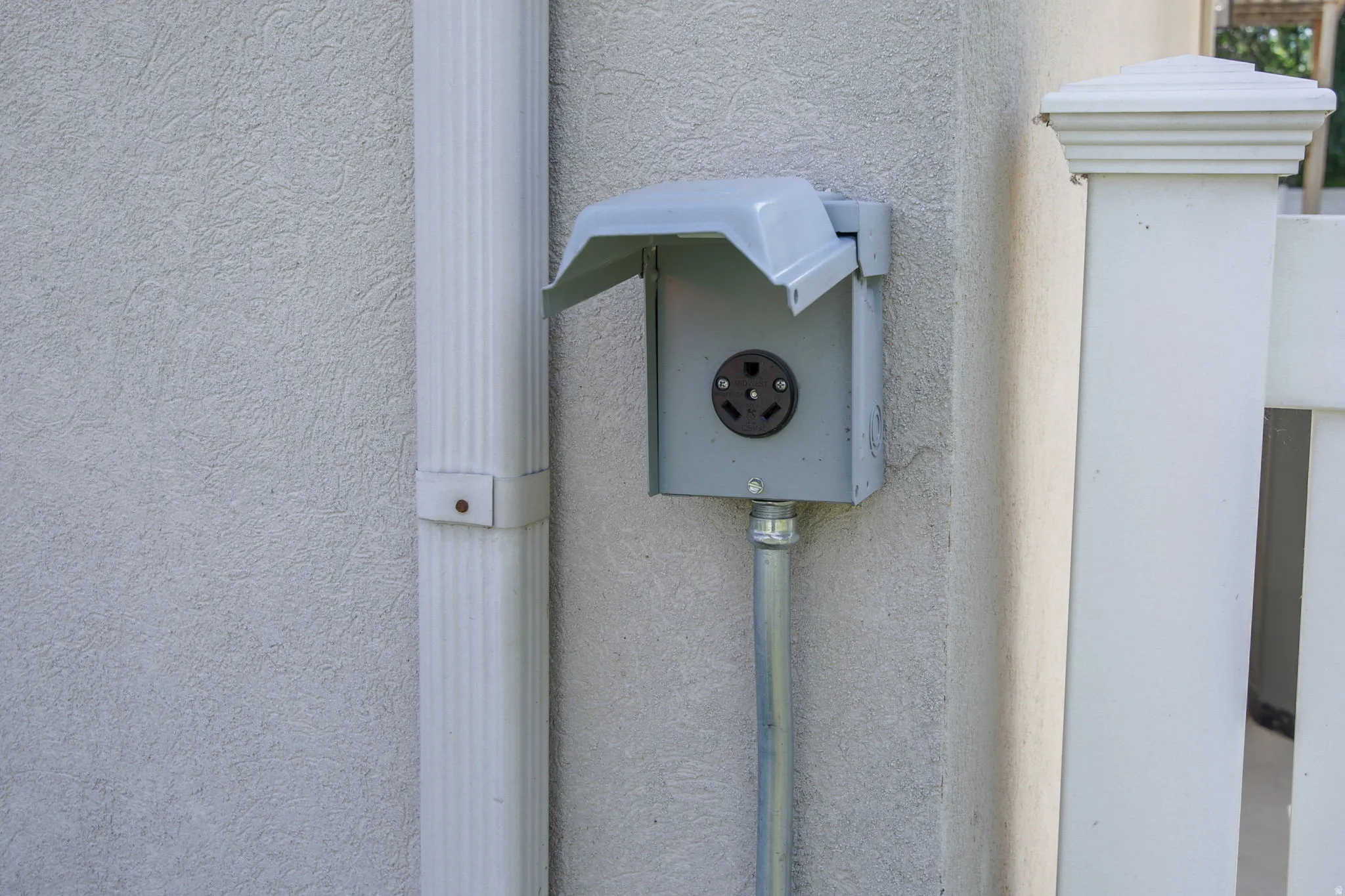 Exterior electrical outlet with weather-resistant cover, metal conduit, and stucco wall finish