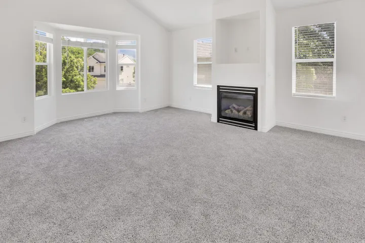 Spacious interior featuring a contemporary fireplace with a black surround, vaulted ceiling, and light gray carpeting