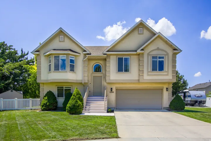 Stucco exterior residence featuring a two-car garage, manicured front lawn, and mature landscaping