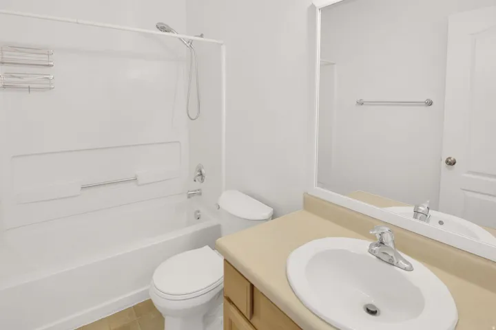 Bathroom featuring a white bathtub with an integrated shower, a toilet, and a vanity with an integrated sink and light-toned countertop