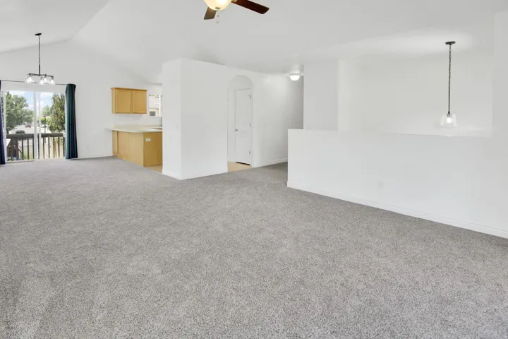 Spacious living area featuring vaulted ceilings, light gray carpet, an overhead ceiling fan, and direct access to an outdoor balcony